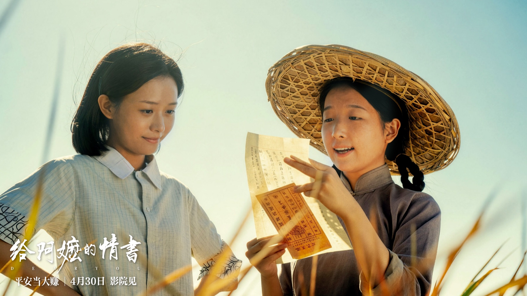 A film still from Dear You showing two young women in a sunlit field, one in a bamboo hat reading a yellow qiaopi remittance letter