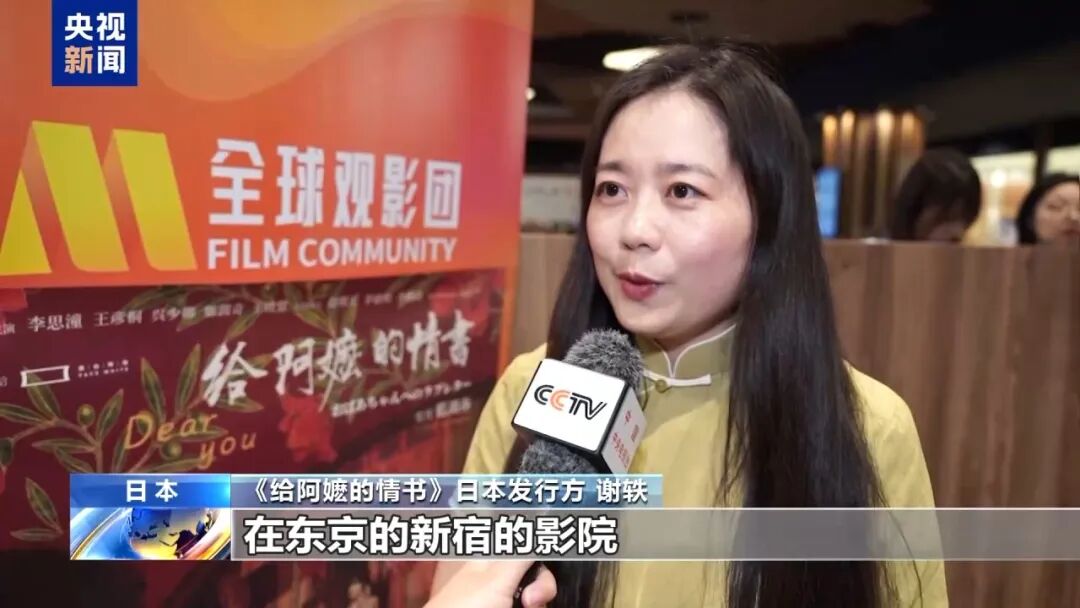 A CCTV News interview with the Japanese distributor of Dear You, standing in front of a film community banner at a Tokyo cinema