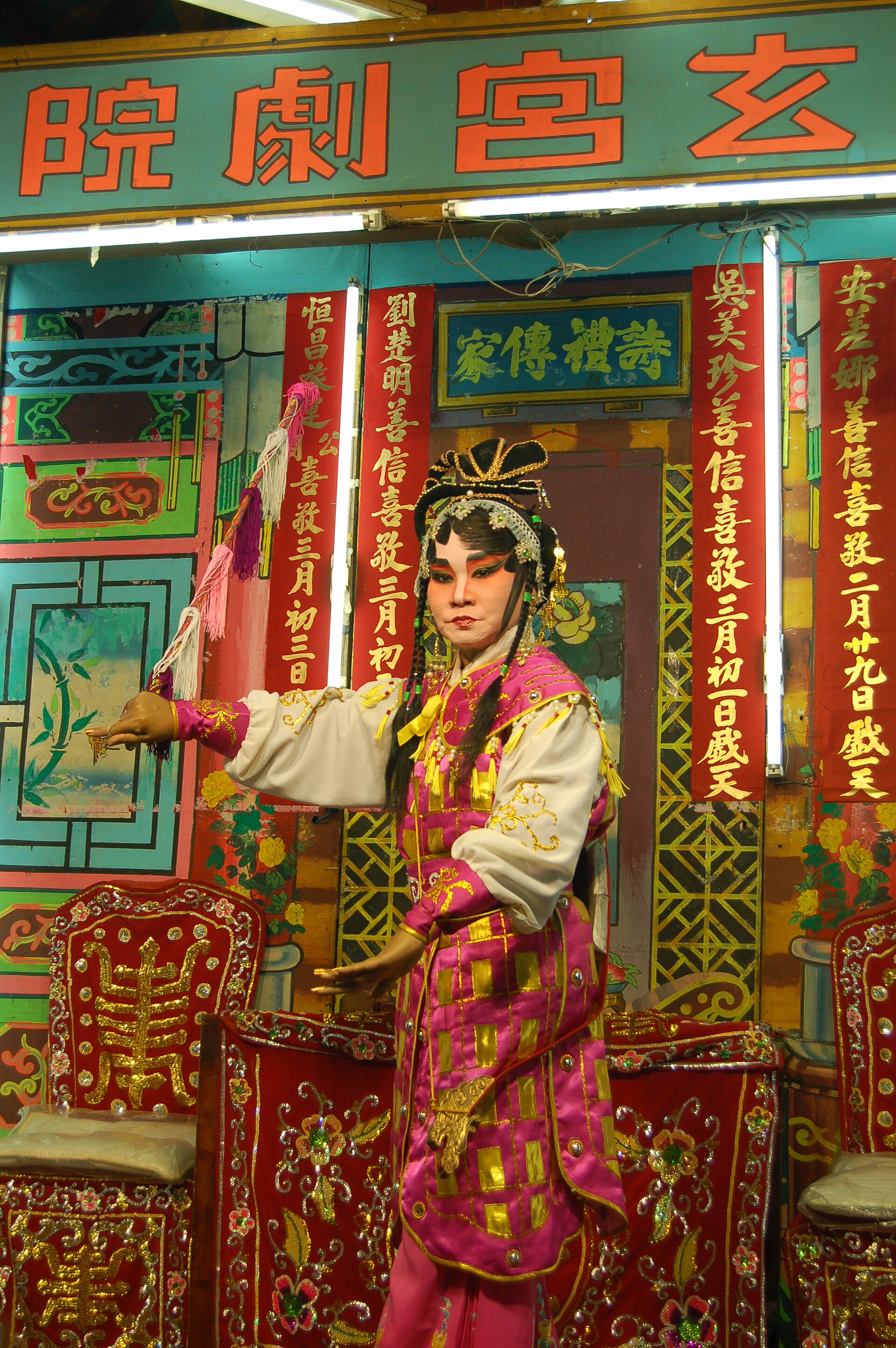 A Teochew opera warrior-role performer holding a staff to represent a horse, in elaborate painted face and headdress